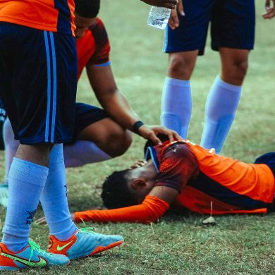 A group of soccer players standing around a man on the ground (Photo: Luis Quintero on Unsplash).