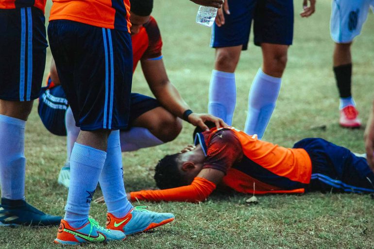 A group of soccer players standing around a man on the ground (Photo: Luis Quintero on Unsplash).